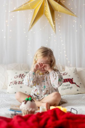 Foto de Pequeño niño rubio, niña, llorando en la cama, no tener regalo para Navidad, imagen triste - Imagen libre de derechos