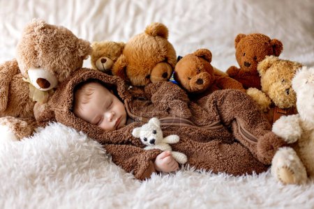 Photo for Sweet new boy child,  baby boy in bear overall, sleeping in bed with teddy bear - Royalty Free Image