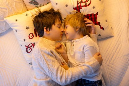 Téléchargez les photos : Doux enfants mignons étonnants, garçons frères, câlins à la maison devant la cheminée à Noël, amour en famille - en image libre de droit