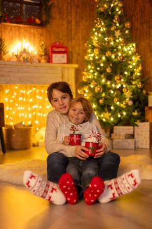 Photo for Sweet amazing cute children, boy brothers, hugging at home in front of the fireplace on Christmas, love in family - Royalty Free Image