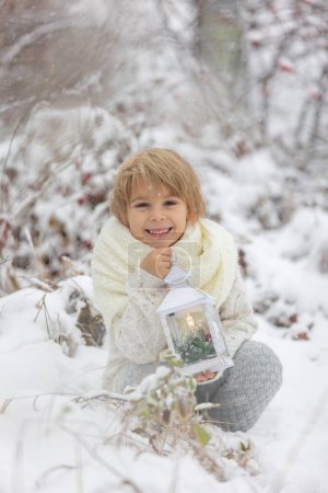 Téléchargez les photos : Mignon petit garçon blond, jouant dans la neige un jour d'hiver, vêtu de chiffons tricotés - en image libre de droit