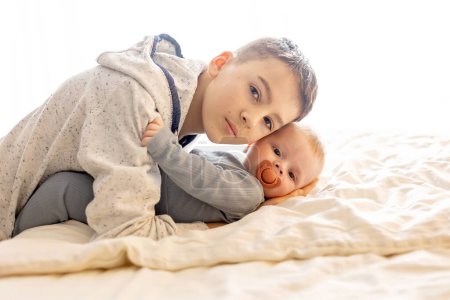 Téléchargez les photos : Preteen enfant, garçon frère, étreignant son petit frère nouveau-né à la maison au lit - en image libre de droit