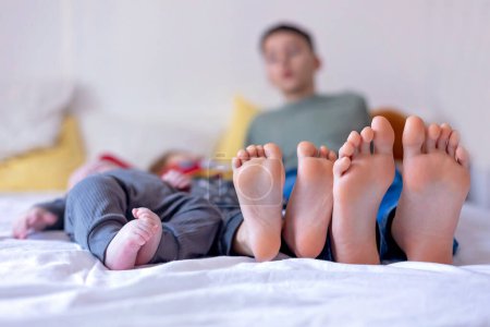 Foto de Chlildren pies, pequeño niño y hermanos mayores pies, bebé se acuesta en la cama por la tarde - Imagen libre de derechos