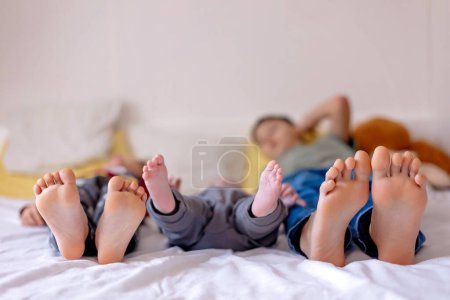 Téléchargez les photos : Enfants pieds, petit garçon et grands frères pieds, bébé couché dans le lit dans l'après-midi - en image libre de droit