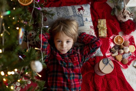 Téléchargez les photos : Enfant mignon, mignon garçon blond, dormir sous le sapin de Noël, attendant le Père Noël la nuit à venir - en image libre de droit