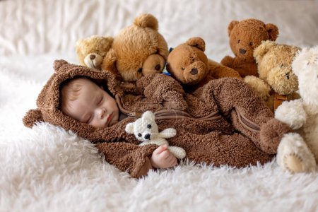 Photo for Sweet new boy child,  baby boy in bear overall, sleeping in bed with teddy bears - Royalty Free Image