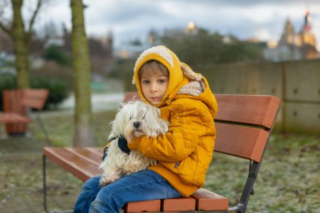 Téléchargez les photos : Mignon écolier, garçon, étreignant son chien de compagnie dans le parc l'hiver - en image libre de droit