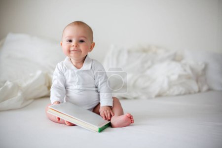 Foto de Lindo niño pequeño en pañal, sonriendo a la cámara en el dormitorio blanco, lindo niño sentado en la cama, sonriendo - Imagen libre de derechos