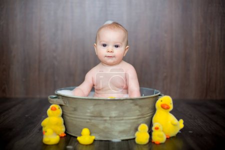 Foto de Lindo bebé jugando con pato de goma mientras está sentado en el lavabo de metal en casa - Imagen libre de derechos