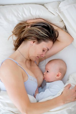 Téléchargez les photos : Jeune mère allaite son bébé, le tenant dans ses bras et souriant de bonheur - en image libre de droit