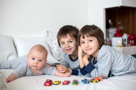 Foto de Tres niños, bebé y sus hermanos mayores en la cama por la mañana, jugando juntos, riendo y divirtiéndose, compartiendo un momento especial, vinculándose - Imagen libre de derechos
