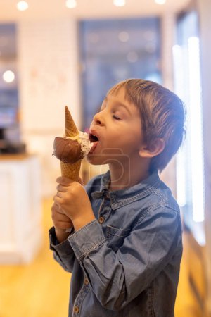 Téléchargez les photos : Mignon garçon doux, enfant, manger de la crème glacée dans un petit magasin de crème glacée hivernale - en image libre de droit