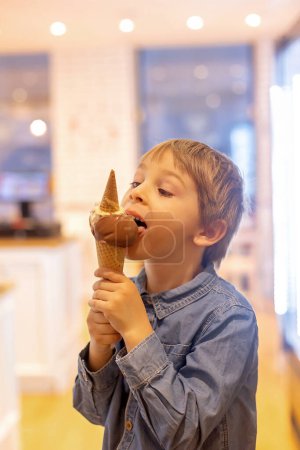 Téléchargez les photos : Mignon garçon doux, enfant, manger de la crème glacée dans un petit magasin de crème glacée hivernale - en image libre de droit