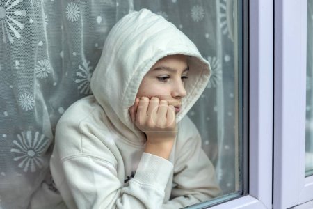 Foto de Retrato artístico de un niño preadolescente, niño, sentado detrás de la ventana, mirando afuera, pensando - Imagen libre de derechos
