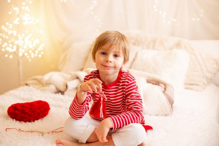 Foto de Lindo niño preescolar, jugando con pulseras blancas y rojas. Martenitsa, cepas blancas y rojas de hilo, tradición folclórica búlgara, primavera de bienvenida en marzo, símbolo de adorno, deseo de buena salud - Imagen libre de derechos