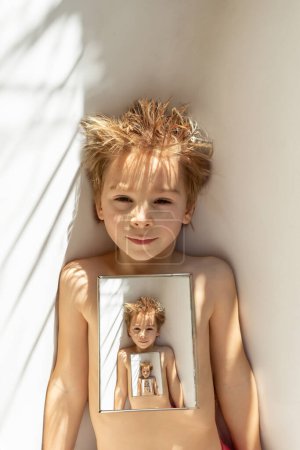 Photo for Cute child, boy, lying in bed with mirror, portrait in the mirror with reflection, sunny weather wintertime - Royalty Free Image