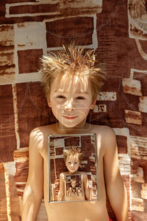 Foto de Lindo niño, niño, acostado en la cama con espejo, retrato en el espejo con reflejo, tiempo soleado invierno - Imagen libre de derechos