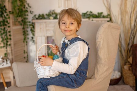 Téléchargez les photos : Doux garçon d'âge préscolaire en studio, jouant avec, oeuf pour Pâques et manger du chocolat, enfant en vacances de Pâques à la maison - en image libre de droit