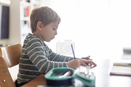 Foto de Niño, chico de la escuela, escribiendo tareas en casa después de la escuela por la tarde - Imagen libre de derechos