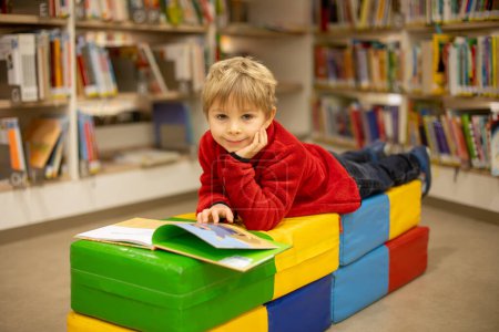 Téléchargez les photos : Adorable little child, boy, sitting in library, reading book and choosing what to lend, kid in book store - en image libre de droit