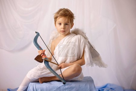 Foto de Little cupid toddle boy, holding bow and arrow, beautiful blond cherub, love - Imagen libre de derechos