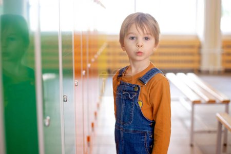 Photo for Sweet blonde toddler boy standing in front of a lockers in kindergarden or school hallway, wintertime - Royalty Free Image