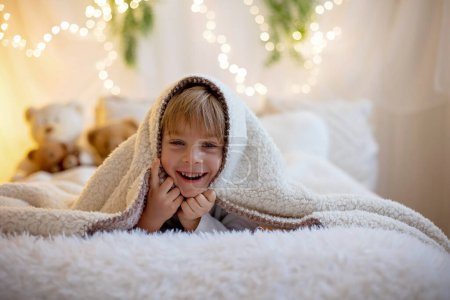 Foto de Pequeño niño preescolar lindo, sosteniendo lindo oso de peluche, escondido bajo el mantel, jugando en casa en el dormitorio soleado - Imagen libre de derechos