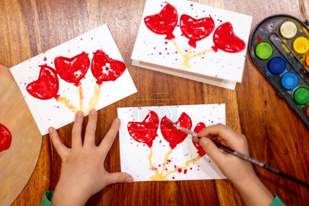 Foto de Niño, hacer una imagen de arte creativo con corazones para San Valentín en casa para una novia - Imagen libre de derechos