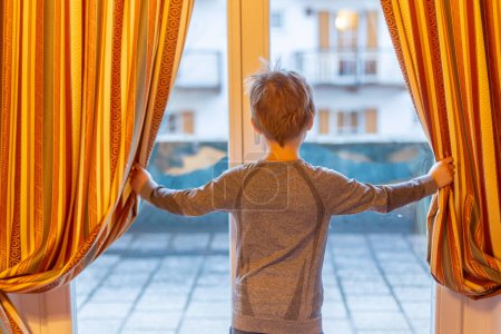 Photo for Child, standing in front of the window in hotel in the mountains, winter ski vacations - Royalty Free Image