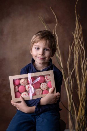 Téléchargez les photos : Belle enfant blonde, garçon, boîte de maintien avec des macarons doux pour la Saint-Valentin - en image libre de droit