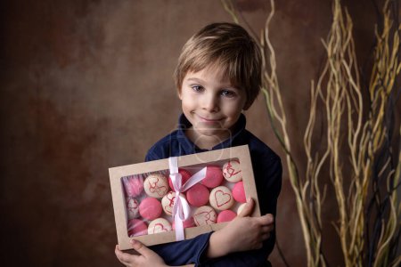 Photo for Beautiful blond child, boy, holding box with sweet macaroons for valentine - Royalty Free Image