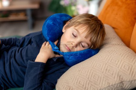Cute blond child, boy, sleeping at home in the afternoon after school with neck pillow, relaxing