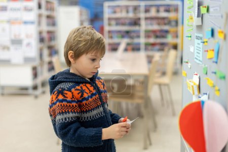 Foto de Niño inteligente, chico de escuela, educándose en una biblioteca, pidiendo prestado libros para leer - Imagen libre de derechos