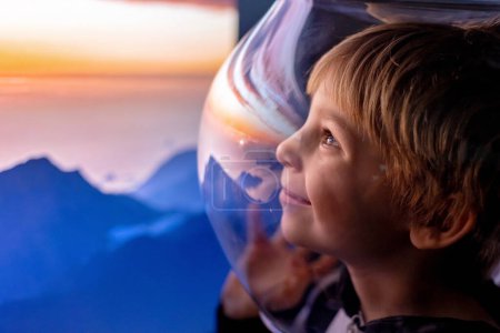 Téléchargez les photos : Enfant mignon, garçon, rêvant de devenir astronaute et de voler dans l'espace. reflet de la lune dans son casque - en image libre de droit