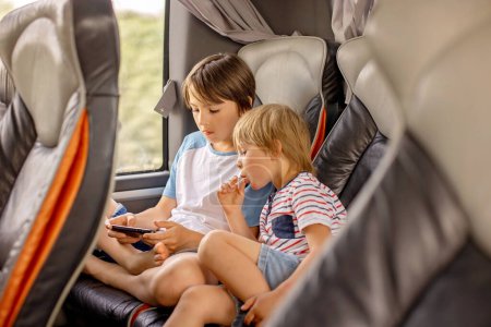 Téléchargez les photos : Enfants, frères et sœurs, jouer sur un téléphone portable pendant un long voyage en bus, vacances en famille - en image libre de droit
