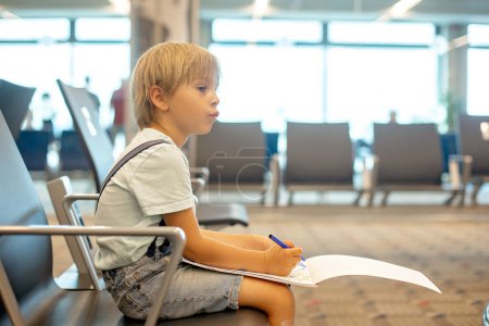 Photo for Child, cute boy, traveling with family, waiting at the airport to board the aircraft, drawing picture in the waiting hall - Royalty Free Image