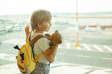 Téléchargez les photos : Enfant, regardant par la fenêtre de l'aéroport les avions, décollant et atterrissant en attendant à bord de l'avion pour des vacances - en image libre de droit