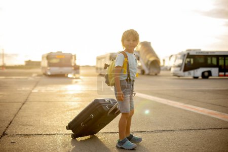 Téléchargez les photos : Mignon enfant blond, enfant avec sac à dos, embarquement à l'aéroport au coucher du soleil, profiter de la vue de l'extérieur - en image libre de droit