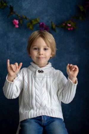 Téléchargez les photos : Mignon petit garçon tout-petit, montrant un geste en langue des signes sur fond bleu, image isolée, enfant montrant des chants de main pour les personnes sourdes - en image libre de droit