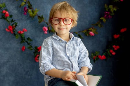 Photo for Cozy spring atmosphere at home, child sitting on chair reading a book, wearing glasses, enjoying - Royalty Free Image