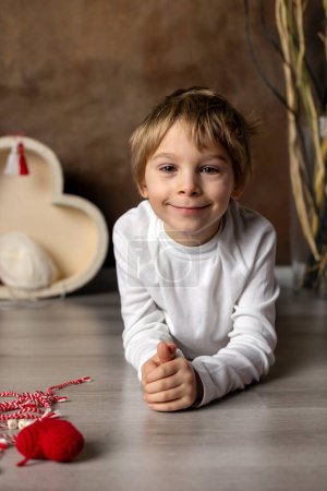 Photo for Cute child, blond boy, playing with white and red bracelet, martenitsa - Royalty Free Image