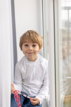 Foto de Niño lindo, niño rubio, jugando con brazalete blanco y rojo, martenitsa - Imagen libre de derechos