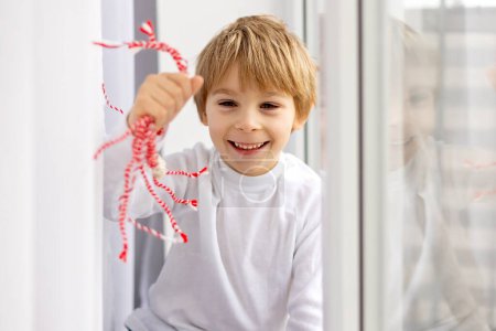 Foto de Niño lindo, niño rubio, jugando con brazalete blanco y rojo, martenitsa - Imagen libre de derechos