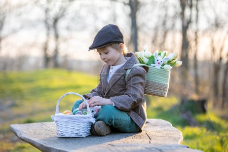 Foto de Hermoso niño pequeño con estilo, niño, jugando con la decoración de Pascua en el parque, primavera al atardecer - Imagen libre de derechos