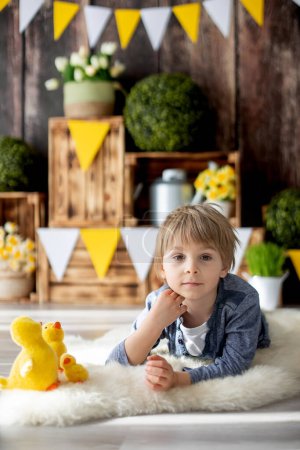 Foto de Lindo niño preescolar joven, niño, jugando con patos en casa, hermosa decoración de primavera para el cumpleaños detrás de él - Imagen libre de derechos