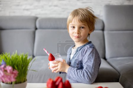 Téléchargez les photos : Doux enfant d'âge préscolaire, garçon, manger des gaufres belges avec des fraises et du chocolat à la maison et smootie driking - en image libre de droit