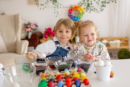 Téléchargez les photos : Happy childen, frères et sœurs, oeufs à colorier avec des eaux colorées pour Pâques à la maison, chambre ensoleillée - en image libre de droit