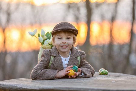 Téléchargez les photos : Beau tout-petit élégant enfant, garçon, jouer avec la décoration de Pâques dans le parc, printemps au coucher du soleil - en image libre de droit