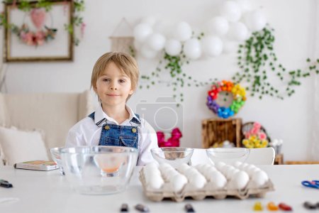 Foto de Feliz niñera, hermanos, huevos para colorear con aguas coloridas para Pascua en casa, sala soleada - Imagen libre de derechos