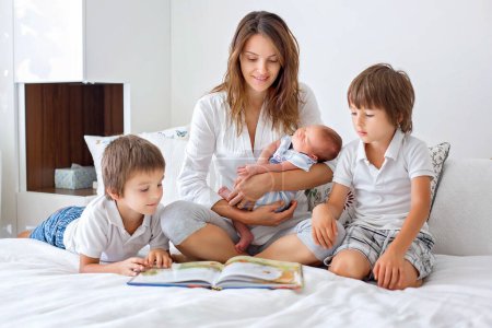 Téléchargez les photos : Jeune mère, lisez un livre à ses trois enfants, garçons, dans la chambre, concept de fête des mères - en image libre de droit